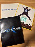 Three press kit folders for the movies Throw Momma From the Train, Jumpin' Jack Flash, and SpaceCamp laid out on table