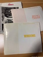 Three press information folders titled "THE FORMULA," "BEING THERE," and "WINDOWS" on a table.
