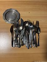 Top down shot of assortment of forks, spoons, knives gathered with decorative plate on wooden surface.