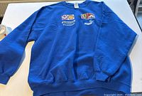 Full view of blue vintage sweater with printed logos from Ferrari, Puma, Shell and M. Schumacher.