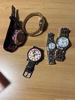 Top view of five watches on a wooden surface showing various styles including analog and digital, metal and leather bands, Mickey Mouse design.