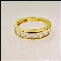 Front-facing view of yellow gold band ring with seven square cubic zirconia stones in channel setting on white background