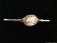 Overview of brooch on black background showing oval shell cameo and gold bar setting
