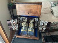 Open wooden case showing four decanters in center and stemmed glasses on side racks