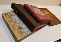 Four Victorian books stacked with spines and decorative covers visible showing titles and wear.