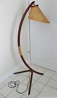 Full view of lamp showing curved teak arm, tripod base, woven shade, jute accent and power cord