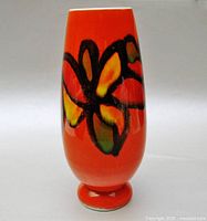 Front view of bright orange Poole Pottery Delphis vase with abstract design in black, yellow, green, and red-orange colors.