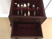 Velvet-lined top drawer showing slots holding assorted silverware pieces
