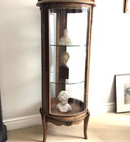 Full view of round curio cabinet showing wood frame, curved glass door and three glass shelves