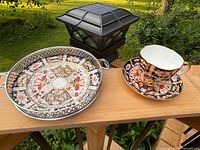 Biscuit/cookie plate and demitasse cup with saucer displayed outdoors on wooden surface with garden background.