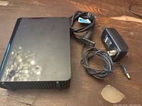 Photo of the top surface and accessories: black external hard drive, power adapter, and USB cable coiled beside it.