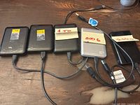 Top view of five Western Digital external hard drives with handwritten capacity labels (1TB, 1TB, 1TB, 500GB, 250GB) and USB cables attached, placed on wooden surface.