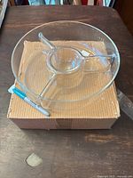 Glass antipasto serving bowl shown resting on its original box with a marker for scale. Transparent glass with a central compartment and three radial divisions visible.