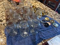 Twenty clear glass small mouth canning jars lined up with assorted metal lids beside them on a blue cloth.