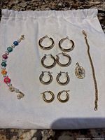 All jewelry pieces including the four pairs of gold-colored hoop earrings, the bracelets, and the pendant arranged on a white cloth.