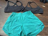 Top view of two black sports bras and one pair of green athletic shorts lying flat on a wooden surface.