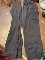 Two pairs of black Nike sweatpants on wooden table, one tight fit mid-rise, one larger with cargo pocket