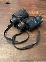Side angle view of Nikon textured black binoculars with neck strap laid on wood surface.