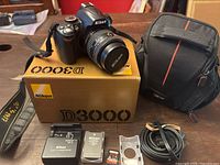 Nikon D3000 camera body with attached lens, Nikon strap, original box and Case Logic bag in background