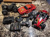 Photo showing all three remote control vehicles and three remote controllers placed on a granite countertop, for parts and untested condition.
