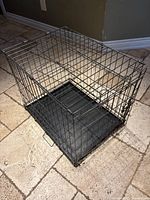 Full assembled metal wire dog crate on stone floor.