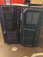 Front view of the pair of black Craig Powerplay 4-way bass reflex speakers with protective grilles over bass drivers and visible mid-range drivers.