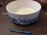 Side view of the hand painted ceramic bowl showing the colorful exterior pattern with pen for scale.