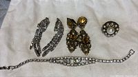 Photo showing all four jewelry pieces laid out on a white cloth: Continental waterfall rhinestone earrings, filigree citrine earrings, Victorian ring with pearl, and rhinestone bracelet.