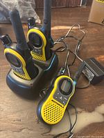 Three yellow and black Motorola walkie talkies placed in and around a single charging base. Charger and antennae visible. Power adapter cable connected.