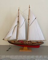Side view of the Bluenose model sailboat showing two masts with white sails, wooden hull with red bottom, and anchor at the bow.