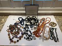 Large lot of costume jewelry featuring multiple beaded necklaces of various colors and styles, bracelets, pendants, a brooch, and a wristwatch displayed on a white background.