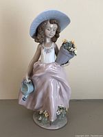 Front and side view of light blue hat, girl holding flower bouquet and watering can, showing glazed porcelain finish and detailed floral decorations.