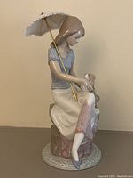 Side angle of the porcelain figurine showing the woman holding a parasol and petting the dog on stacked books.