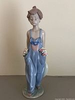Front view of the Lladro figurine showing the child in blue overalls holding flowers in both hands.