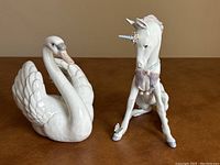 Front view of both porcelain figurines showing swan on left and seated unicorn on right
