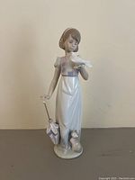 Full front view of Lladró Summer Stroll figurine showing girl with a bird on her hand, umbrella in other hand, and cat at feet.