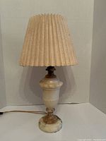 Marble table lamp with beige pleated fabric shade, front view against white background showing full lamp.