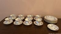 Full set layout showing 8 tea cups, 8 saucers, 8 dinner plates, and one extra saucer all with floral rose pattern and gold trim