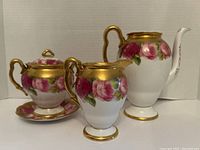 Front view of sugar bowl with lid on saucer, creamer and teapot