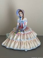 Front view of the seated porcelain figurine showing the full dress and bonnet.