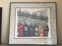 Full view of framed signed print titled 'Osgoode Newsboxes Toronto' depicting various colorful newsboxes in Toronto with architectural background and decorative wrought-iron fence.