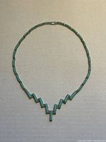 Full view of the turquoise inlaid sterling silver necklace laid flat on a neutral background showing the symmetrical design and clasp.