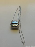 Front and top view of the miniature basket weave coin purse pendant on a linked silver chain, showing the overall shape and detailing of the piece.