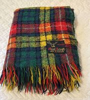 Folded tartan mohair blanket showing label and fringe tassels, vibrant plaid colors of green, red, yellow, black.