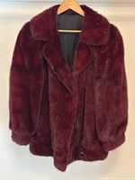 Full front view of dyed red mink fur coat on wooden hanger