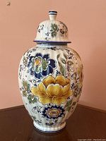 Front side view of the lidded porcelain vase showing detailed hand-painted floral patterns in yellow and blue with green leaves.