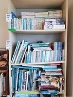 Three wooden shelves densely filled with an assortment of books mostly arranged vertically, with some stacked horizontally on the middle and bottom shelves.
