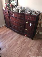 Full view of the wooden sideboard cabinet showing curved drawers and cupboard doors with brass handles, along with various dishes on top.