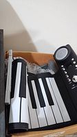 Close-up of flexible roll-up keyboard with black and white keys, attached speaker, volume knob, and buttons.