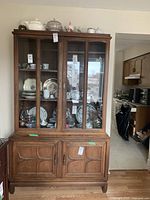 Front view of the china cabinet showing glass doors on upper section with various plates and decorative items inside, closed lower wooden cabinets and drawers.